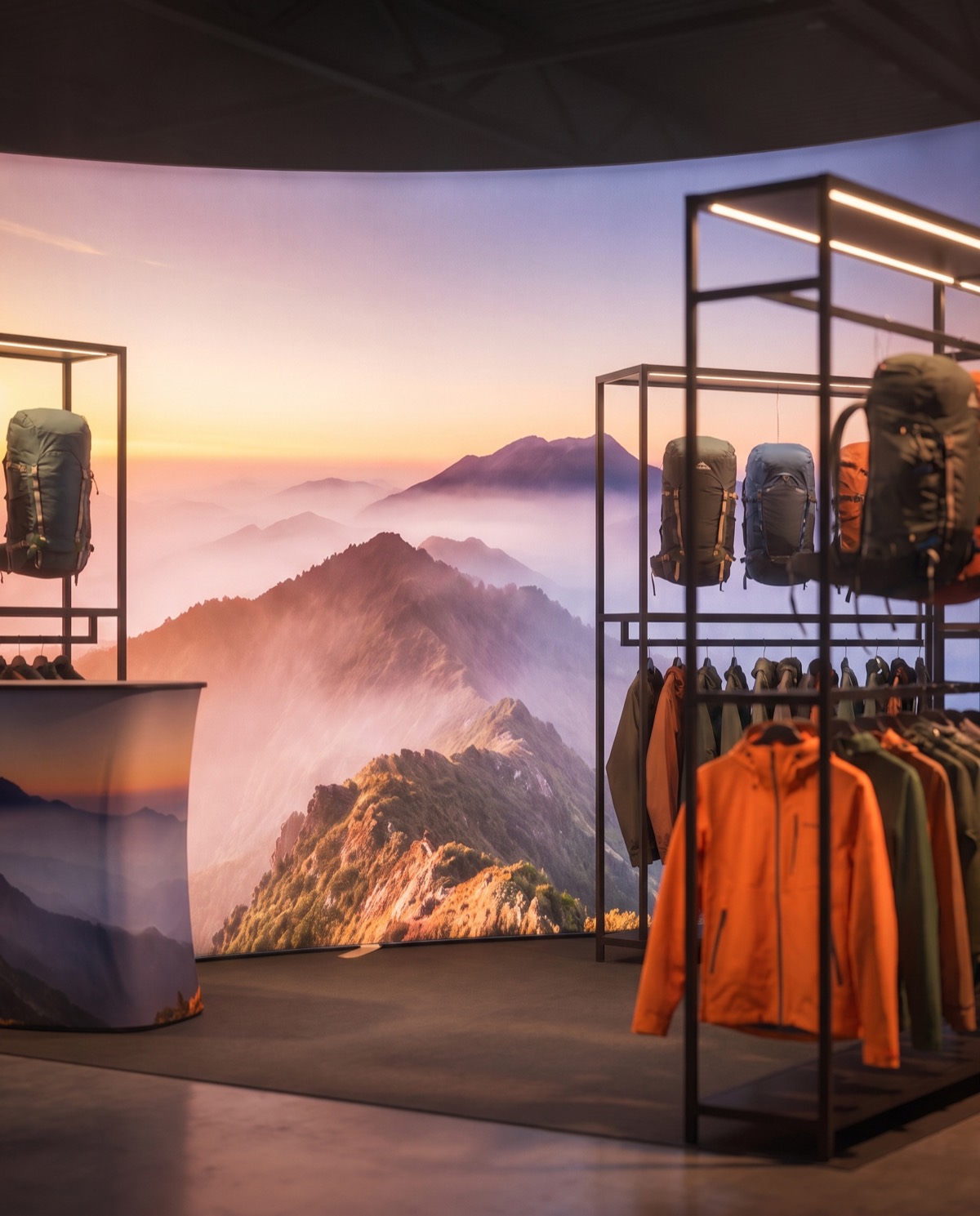 Close-up render of a backlit mountain-landscape fabric wall framing black shelving with backpacks and an orange jacket